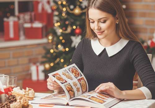 девушка за столом ищетв книге рецепты новогодних блюд