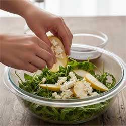 выкладывают в миску руколу, сыр и ломтики груши